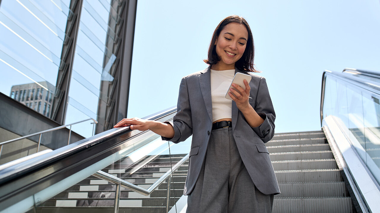 Jeune femme souriante sur un escalator regardant son smartphone